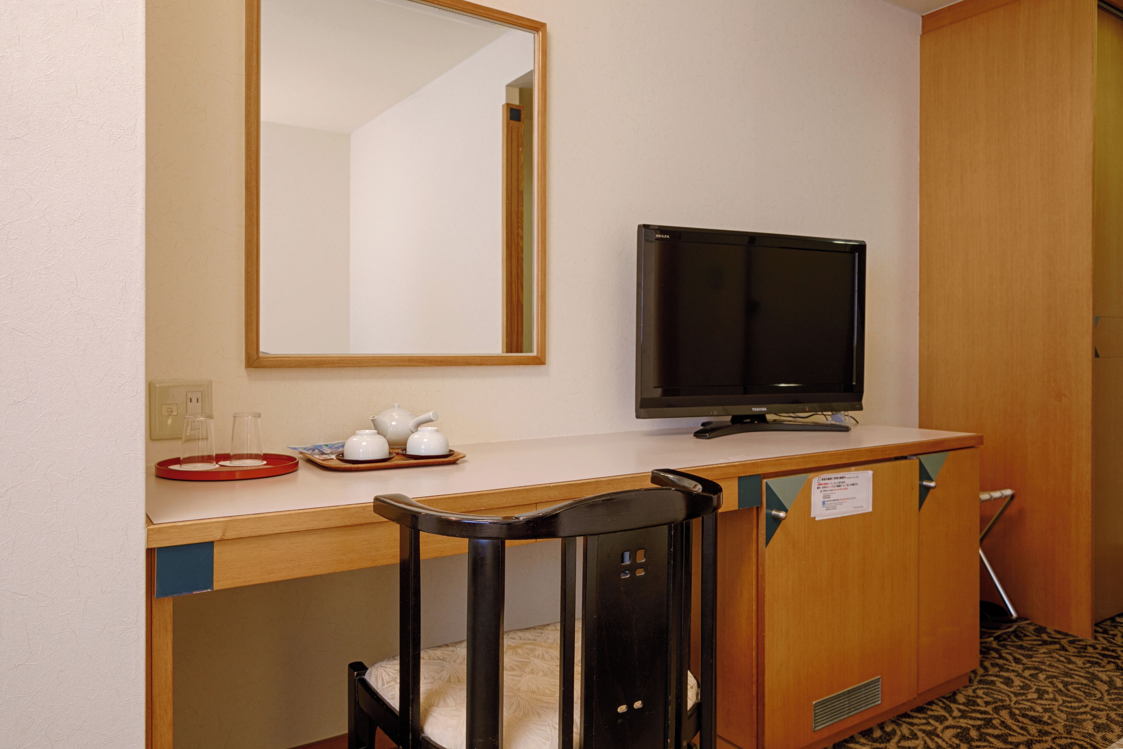 Una habitación de hotel compacta con un escritorio de madera, televisión, una silla y un espejo.