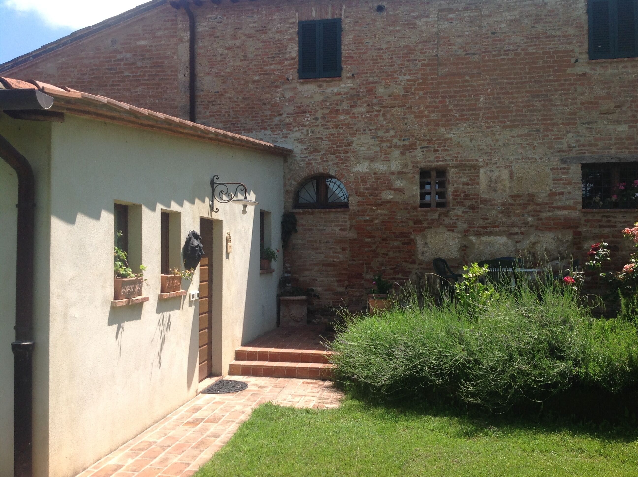 A rustic building with a brick facade, a small porch, and a garden area with plants and flowers.