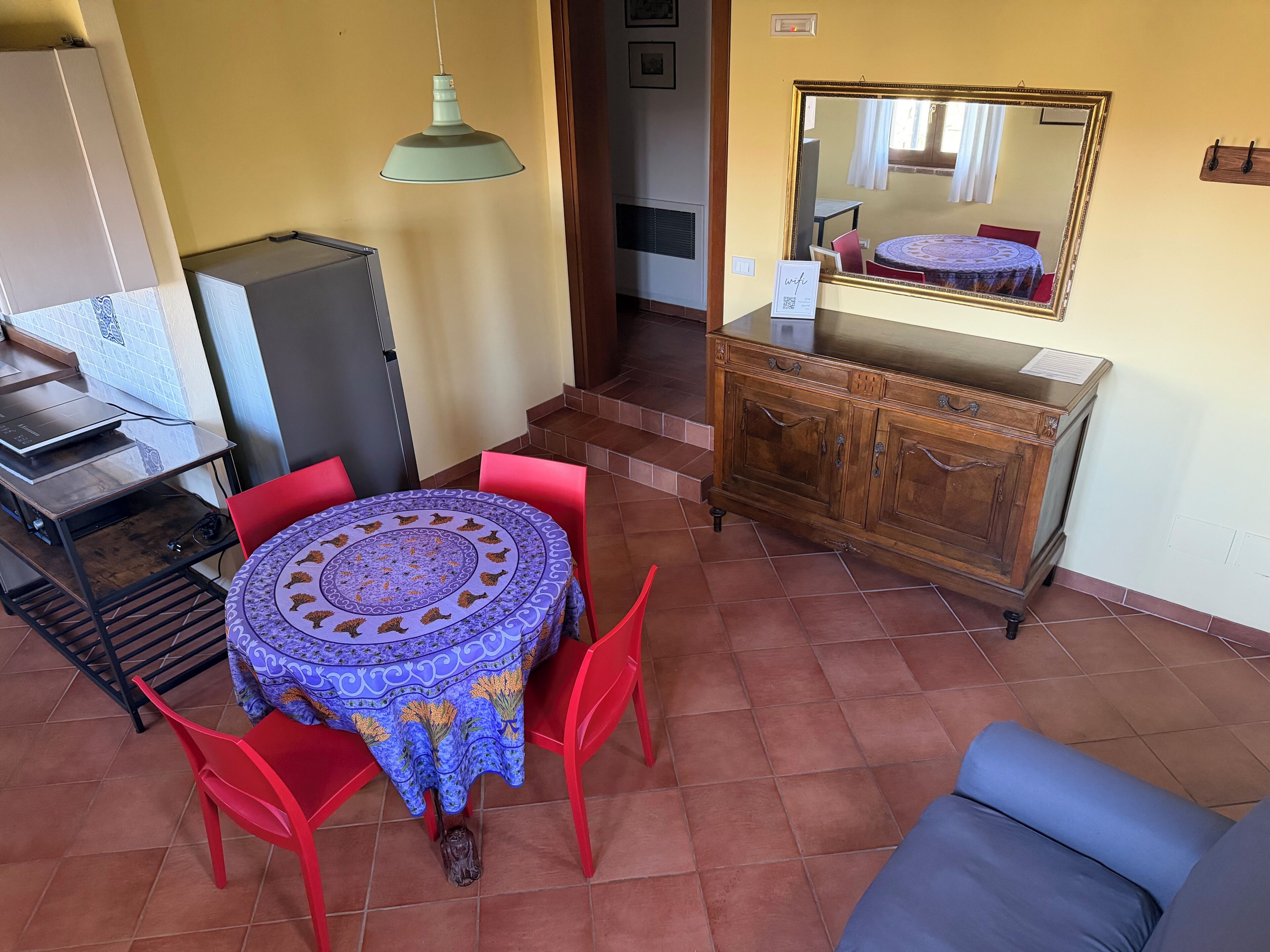 Un coin repas avec une table ronde, des chaises rouges, un buffet en bois et un miroir au mur.