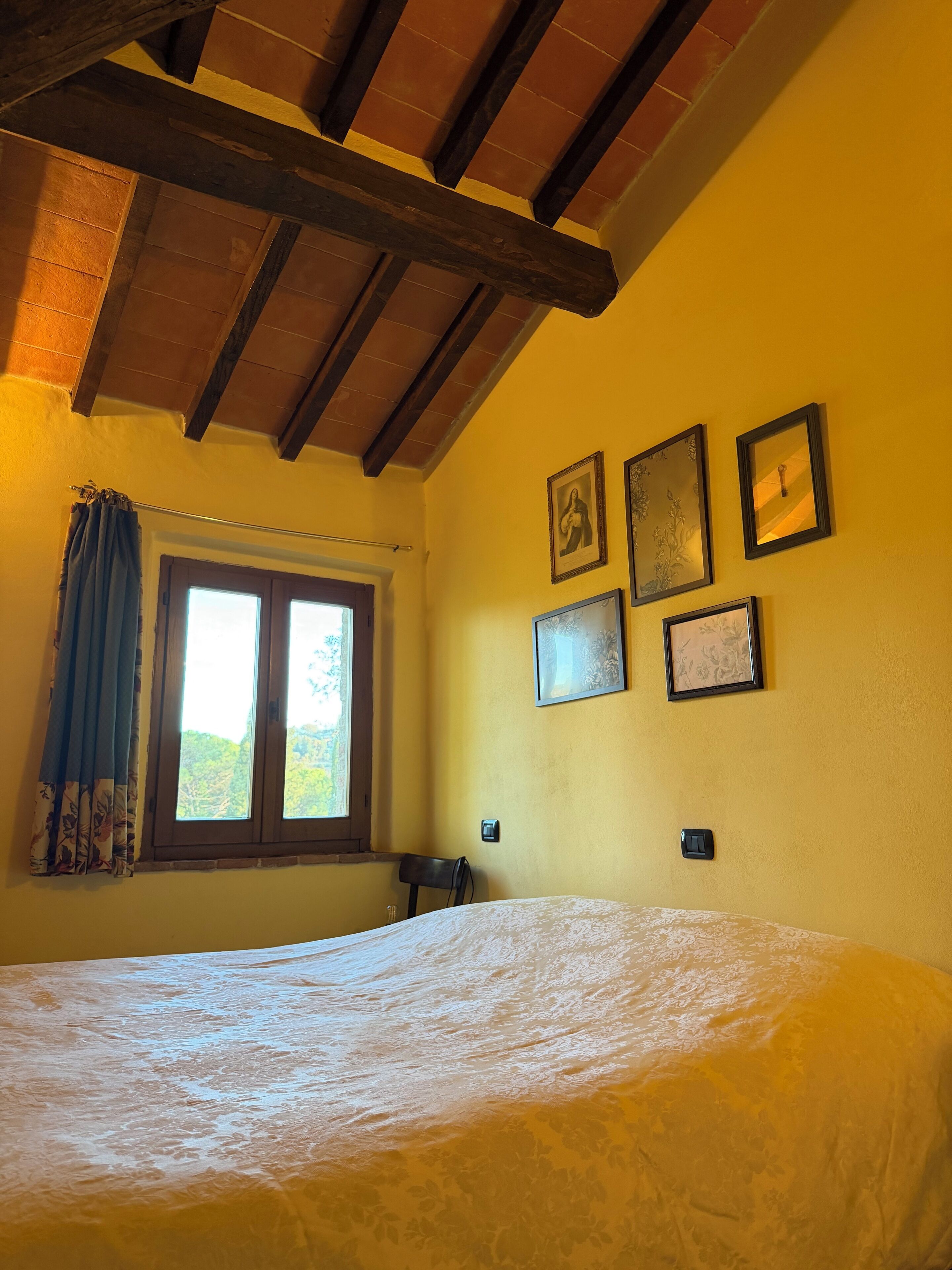Une chambre à coucher avec un lit, une fenêtre avec des rideaux et des tableaux encadrés accrochés au mur.