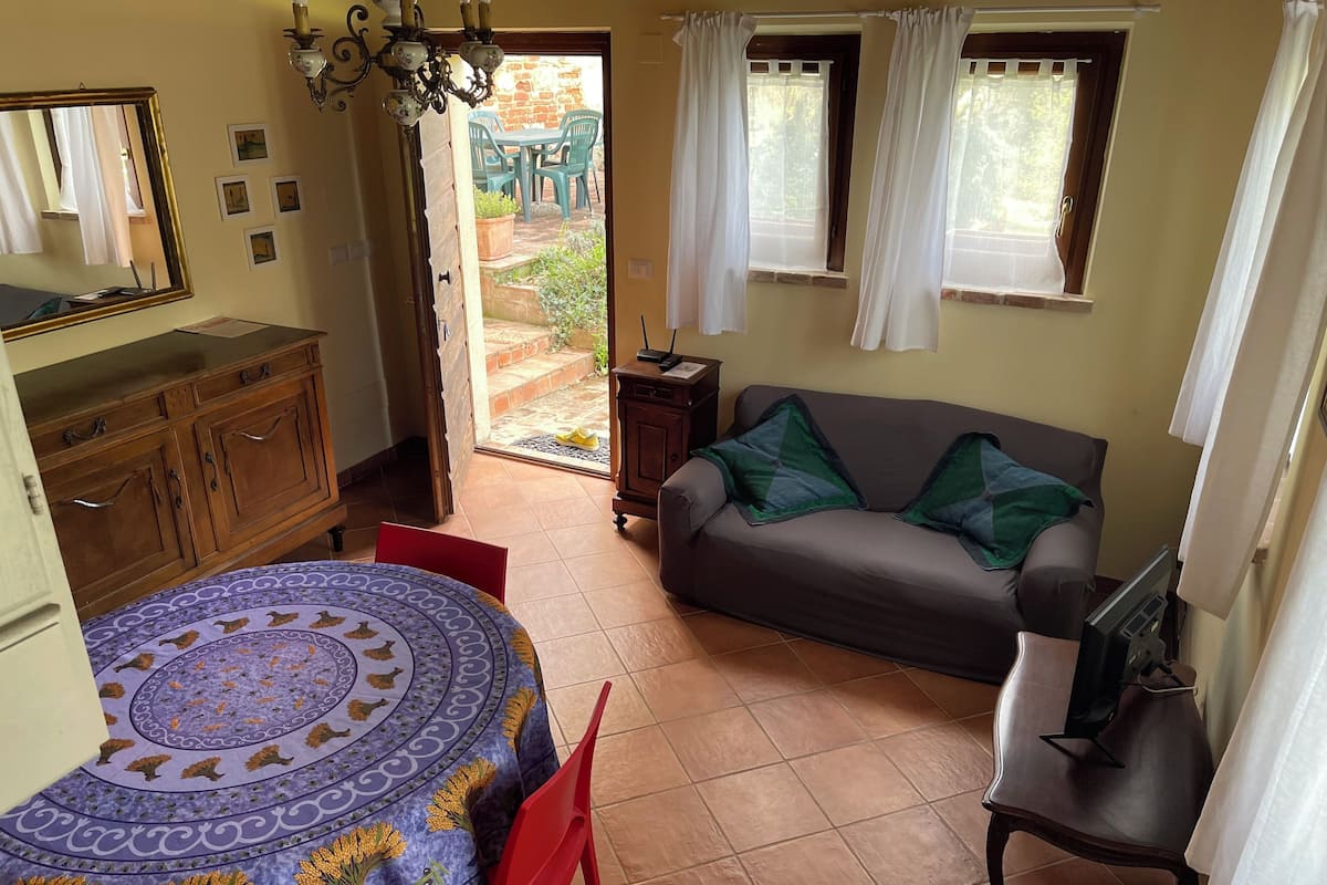 A room with a dining table, a sofa, a TV stand, and a view of the outside.
