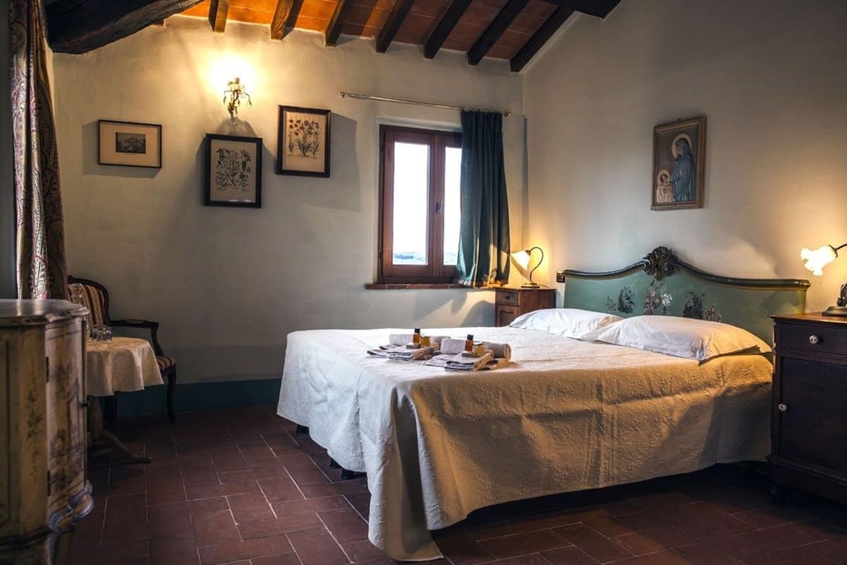 A bedroom with a large bed, a wooden headboard, a window with curtains, and a wall-mounted lamp.