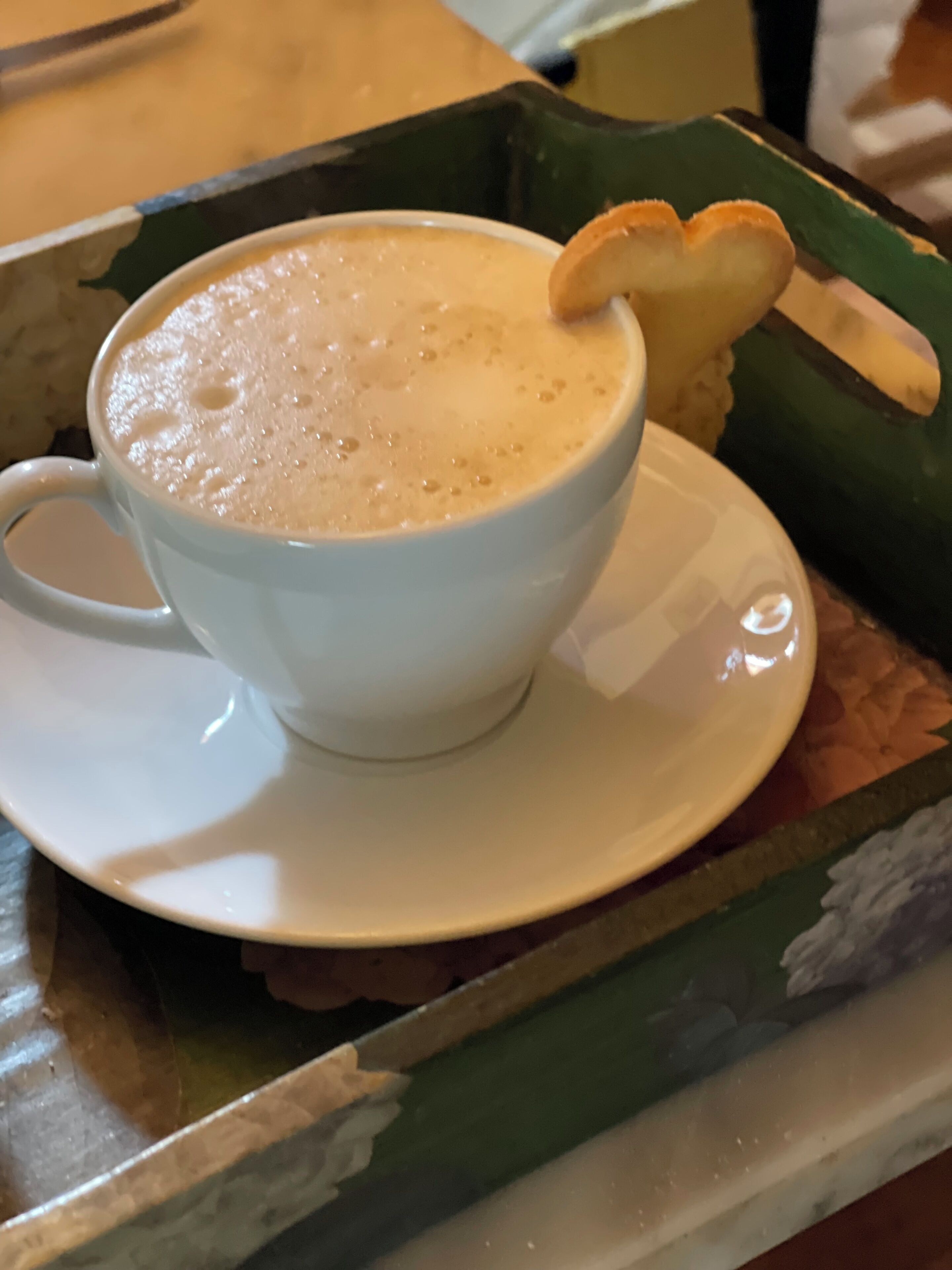 A white cup of coffee with foam on top, placed on a white saucer.