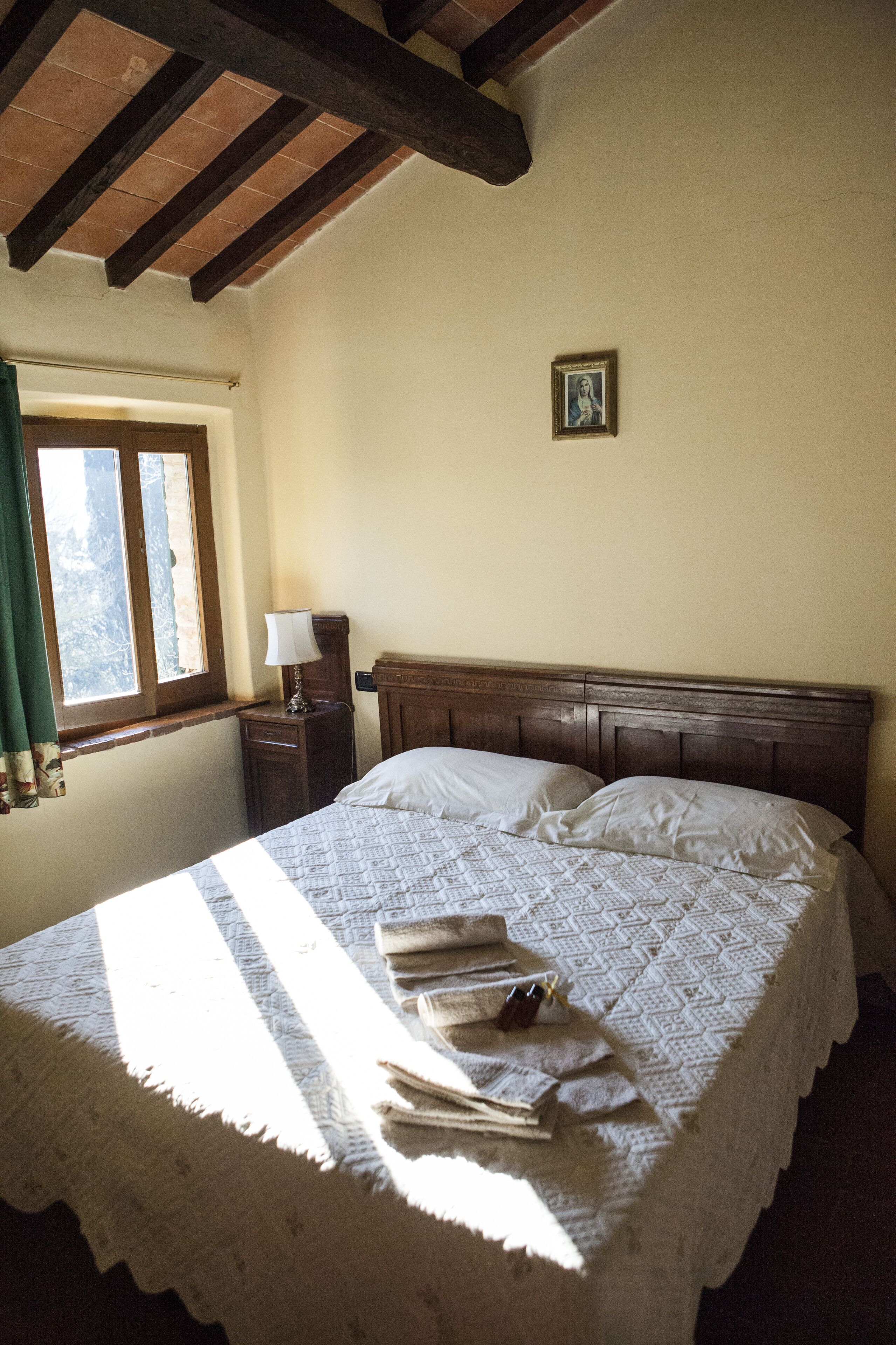 Une chambre à coucher avec une tête de lit en bois, une table de chevet avec une lampe et une fenêtre avec des rideaux.