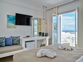 Une chambre d’hôtel moderne équipée d’un lit, d’un coin salon, d’un minibar, d’une télévision et d’un balcon avec vue sur la mer.
