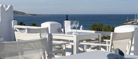 A white outdoor seating area with a table and chairs, a bottle, and two glasses on the table.