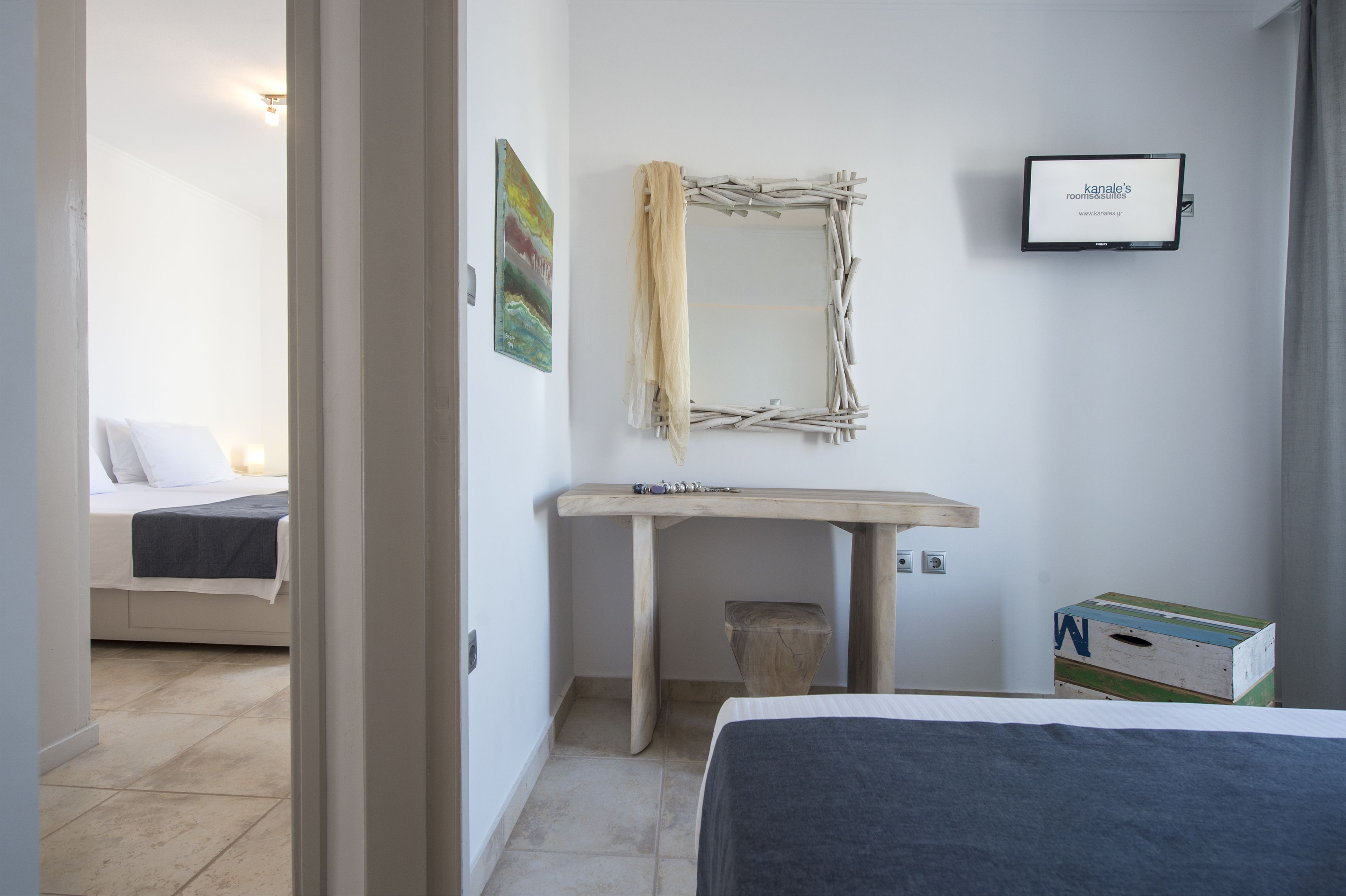 A bedroom with a bed, a wooden desk, a mirror, a television, and a small box.