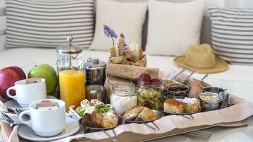 A breakfast tray with various foods and drinks on a bed with striped pillows.