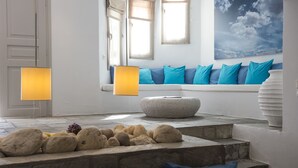 A modern interior with a stone bench, a white door, and a window with blue cushions. - Kanale's Rooms and Suites (Paros)