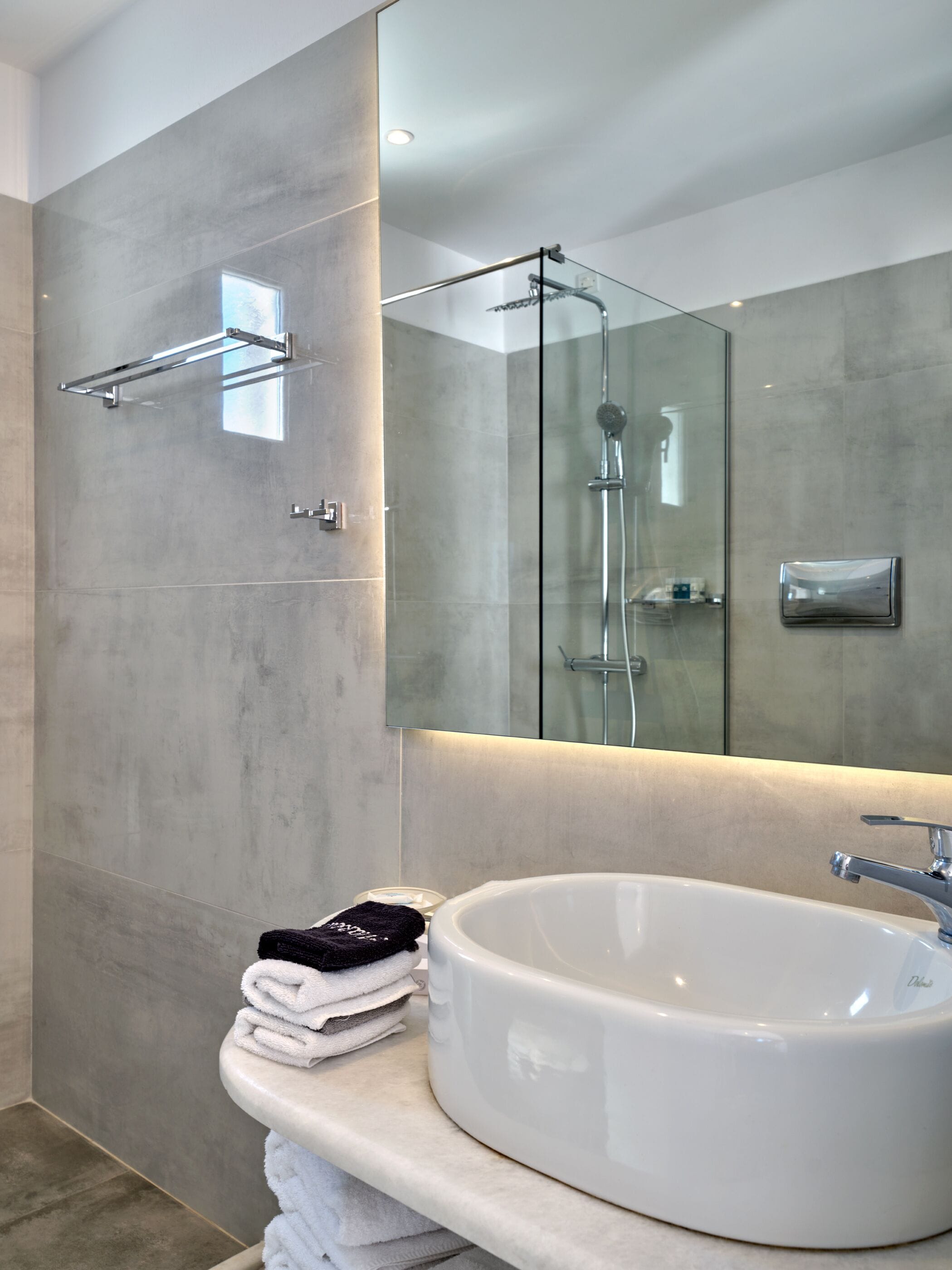 Un baño moderno con un espejo grande, un lavabo redondo y una cabina de ducha de cristal.