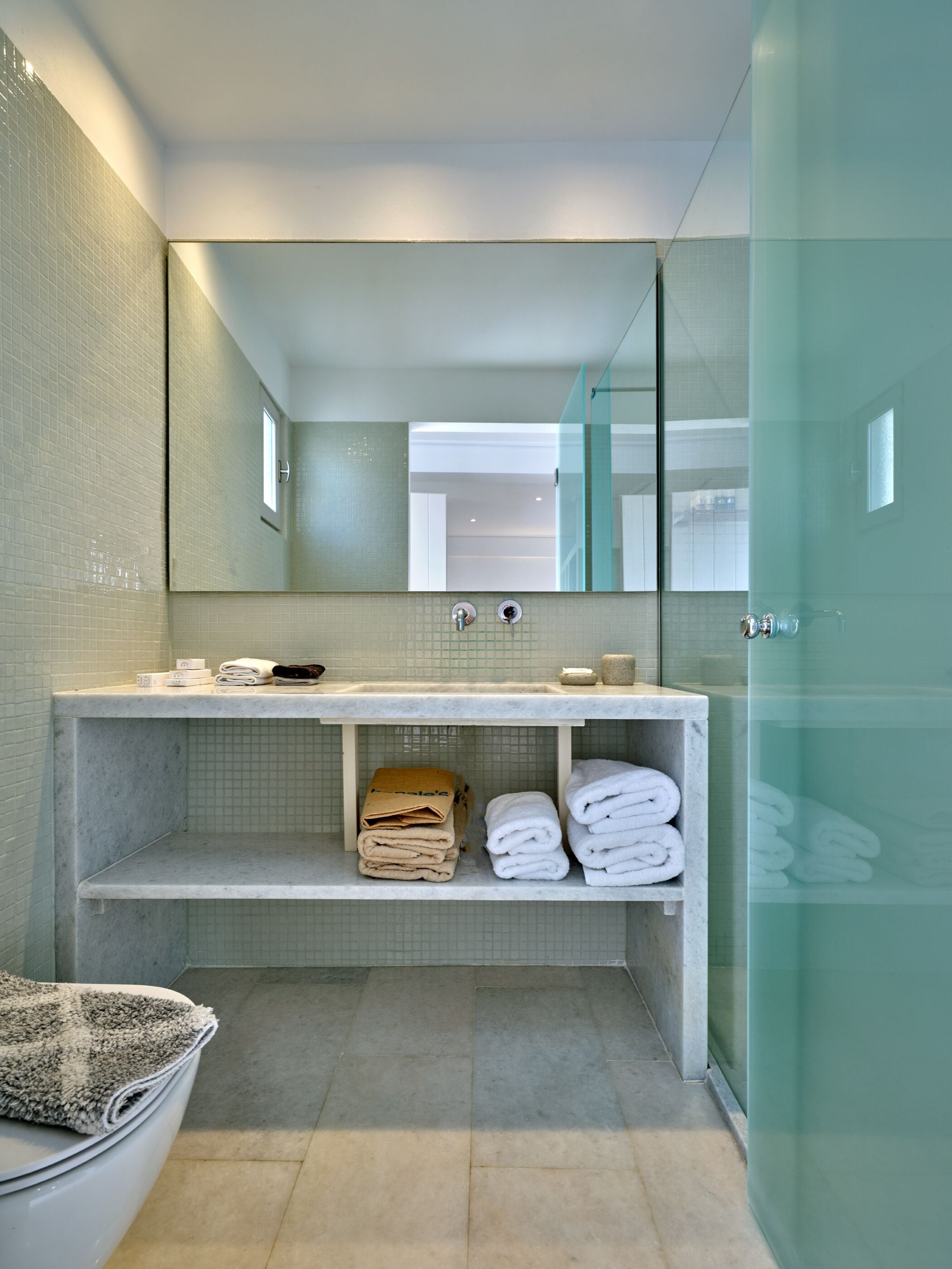 A modern bathroom with a glass shower enclosure, a marble vanity, and neatly folded towels.