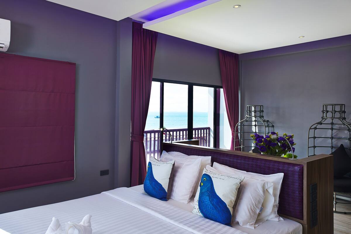 Una habitación de hotel moderna con una cama grande, un balcón con vistas y una pequeña zona de estar con flores.