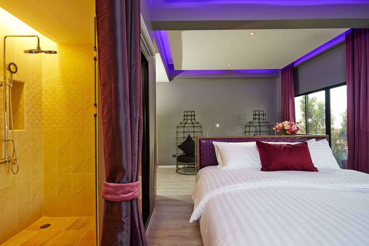 Una habitación de hotel moderna con una cama grande, zona de ducha y vistas al exterior.