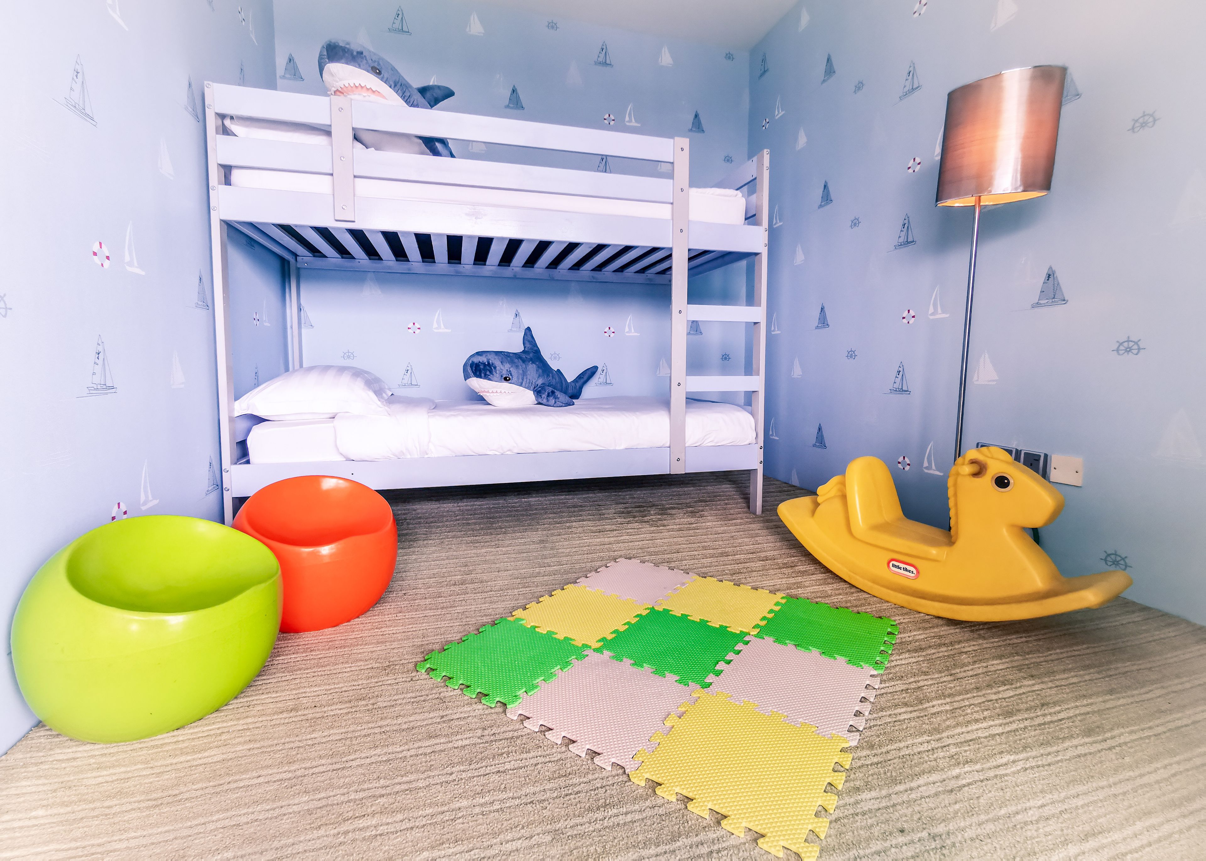 Una cama litera infantil con un peluche de tiburón, una lámpara y un caballito mecedor.