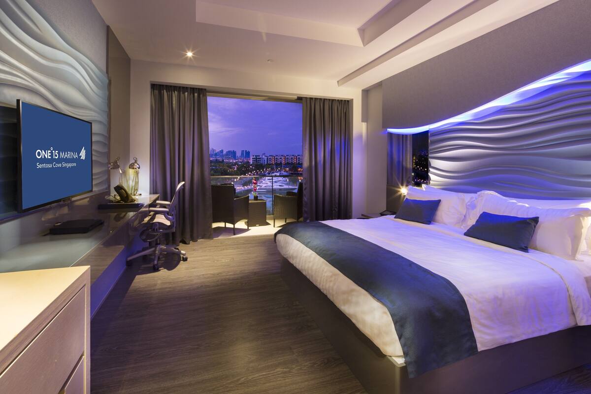 Une chambre d’hôtel moderne, dotée d’un grand lit, d’un bureau et d’un téléviseur affichant le nom de l’hôtel.
