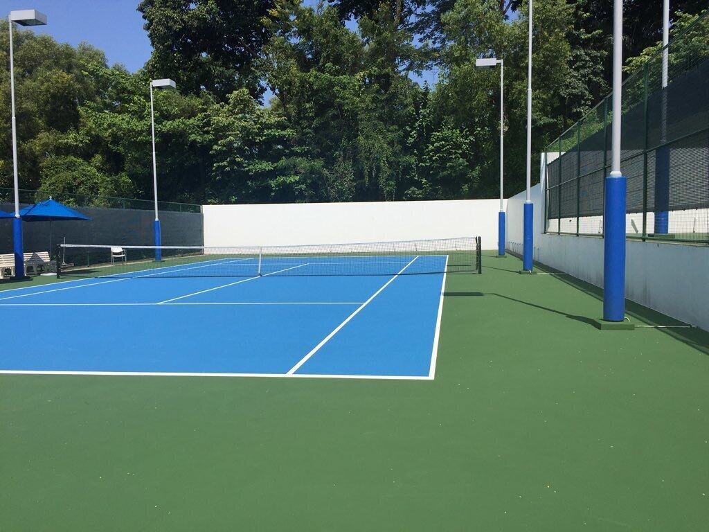 Cancha de tenis al aire libre con red, rodeada por una valla y árboles.