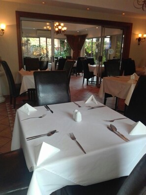 A dining area with tables set for four, each with white tablecloths, silverware, and salt and pepper shakers. Chairs are arranged around the tables. - Elizabeth Lodge (Boksburg)