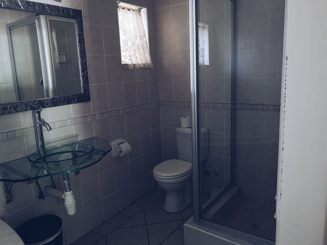 Casa de banho com lavatório de vidro, sanita e zona de duche.