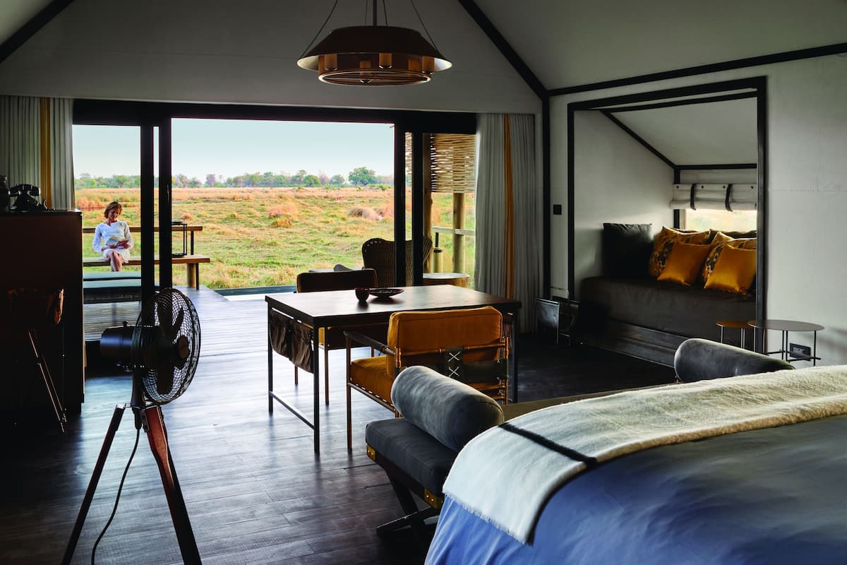 A room with a bed, a table, and a chair, with a view of a field through the window.