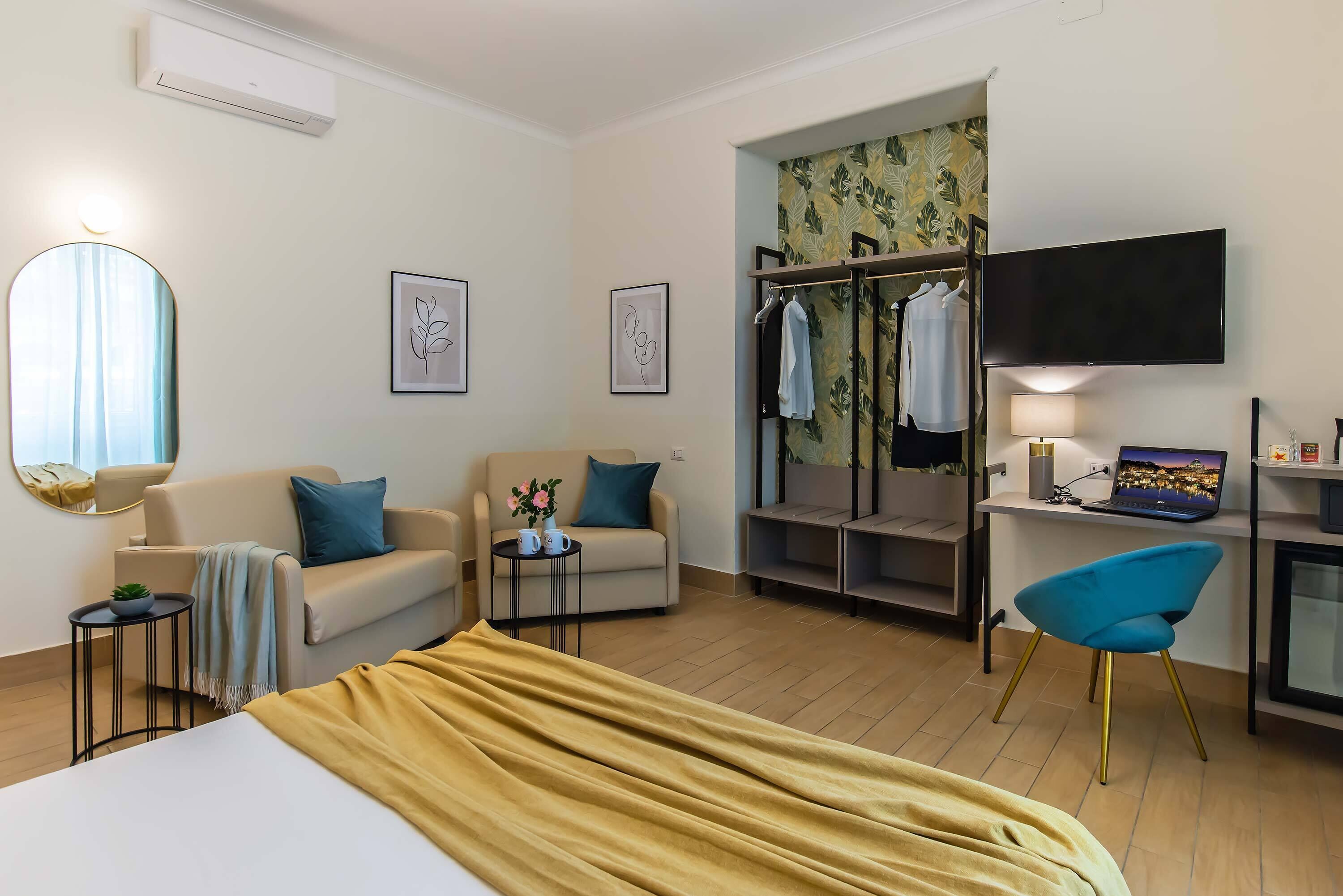 Una camera d'albergo con un letto, un divano, una scrivania con un portatile, una TV e un armadio.