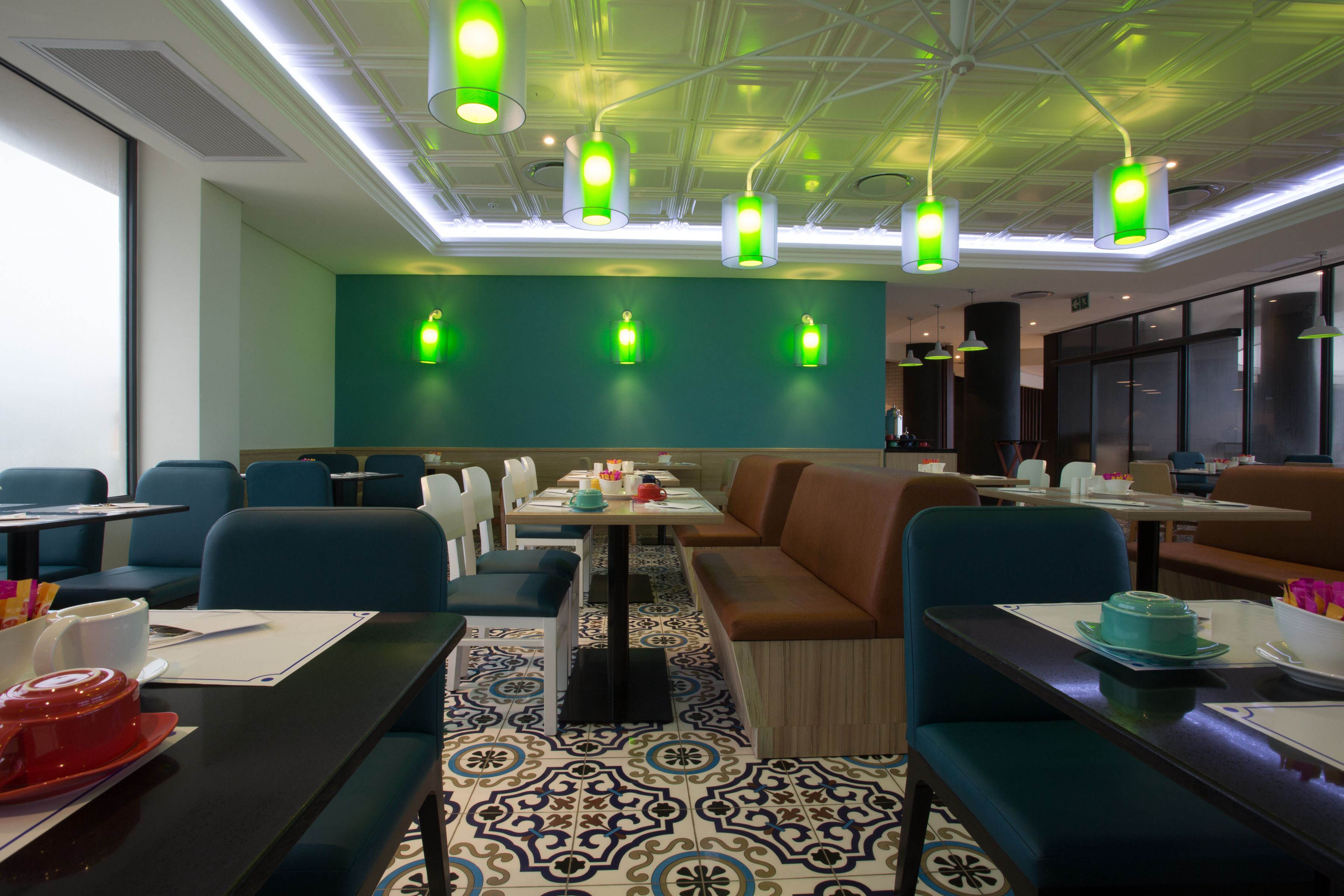 A modern restaurant with blue and brown seating, patterned floor tiles, and green pendant lighting.