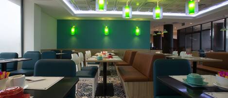A modern restaurant with blue and brown seating, patterned floor tiles, and green pendant lighting.