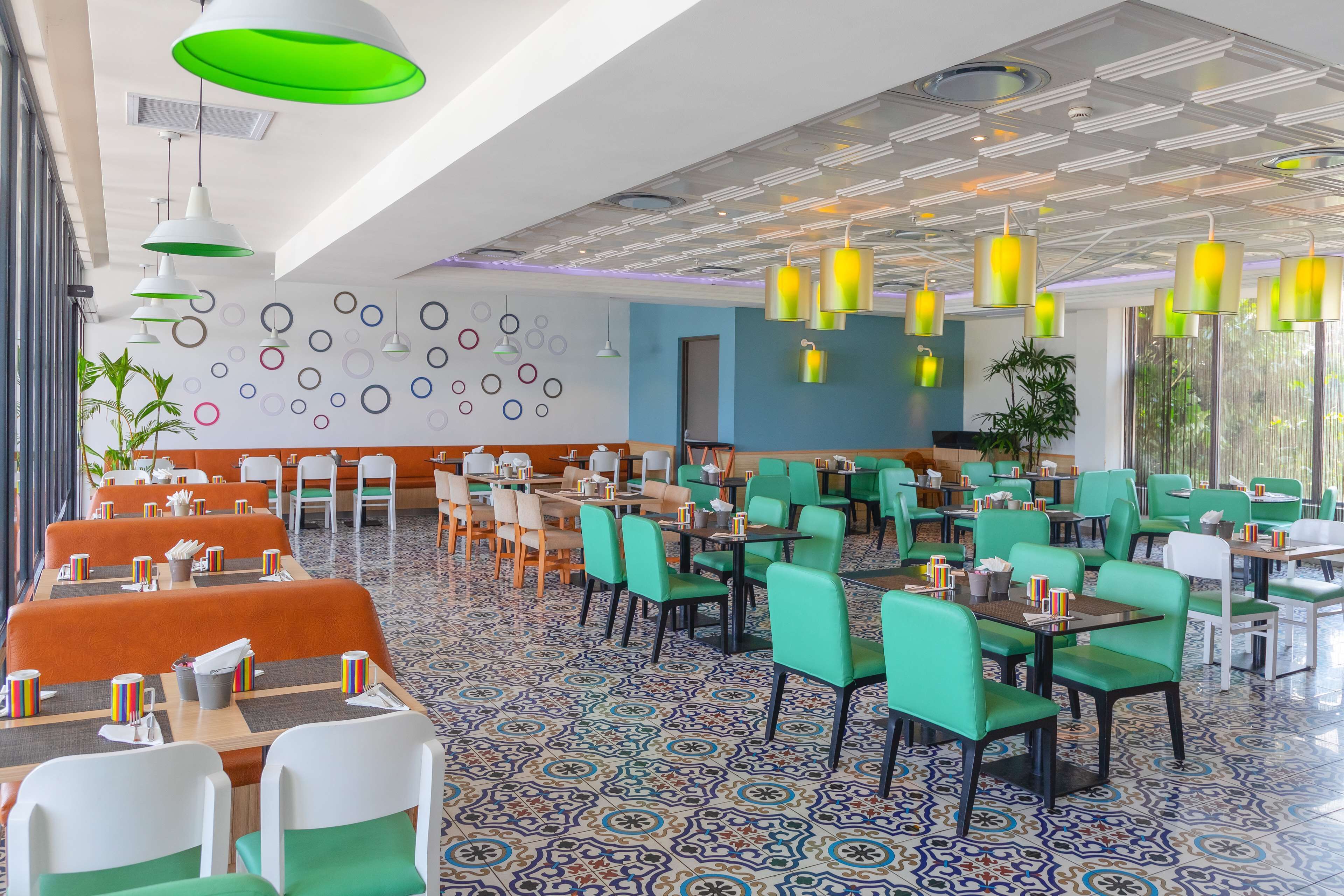 Ein geräumiges Restaurant mit grün-weißen Sitzmöglichkeiten, gemusterten Bodenfliesen und moderner Pendelleuchten.