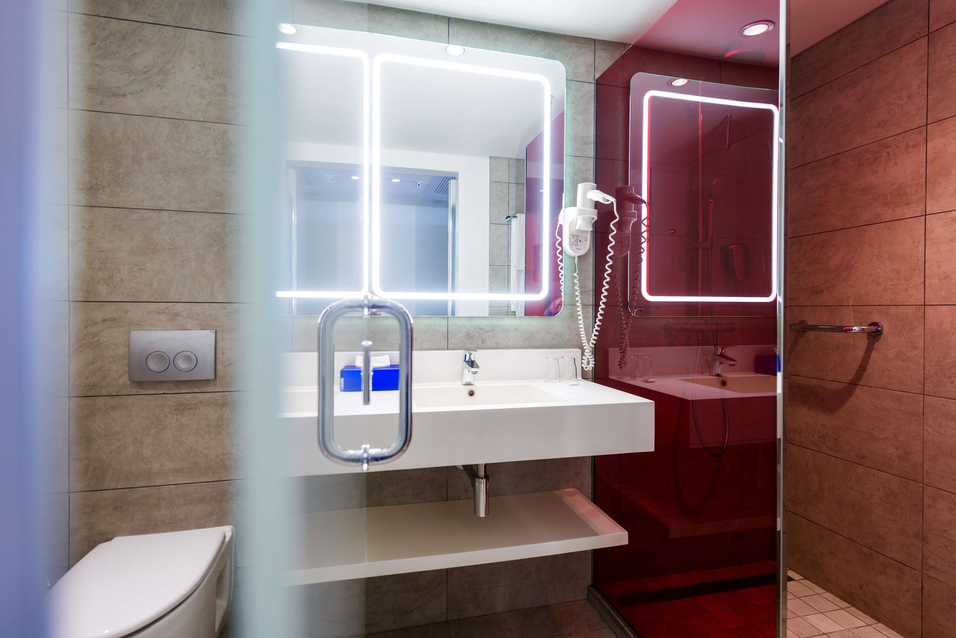 Ein modernes Badezimmer mit einem weißen Waschbecken, einer Duschkabine aus Glas und einem Spiegel mit Neonbeleuchtung.