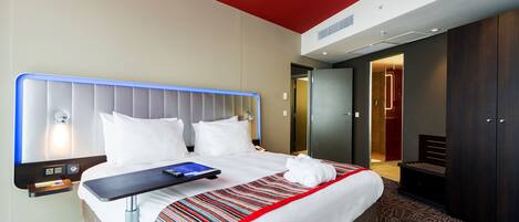 Una habitación de hotel con una cama grande, una mesita de noche con un control remoto y un techo rojo.