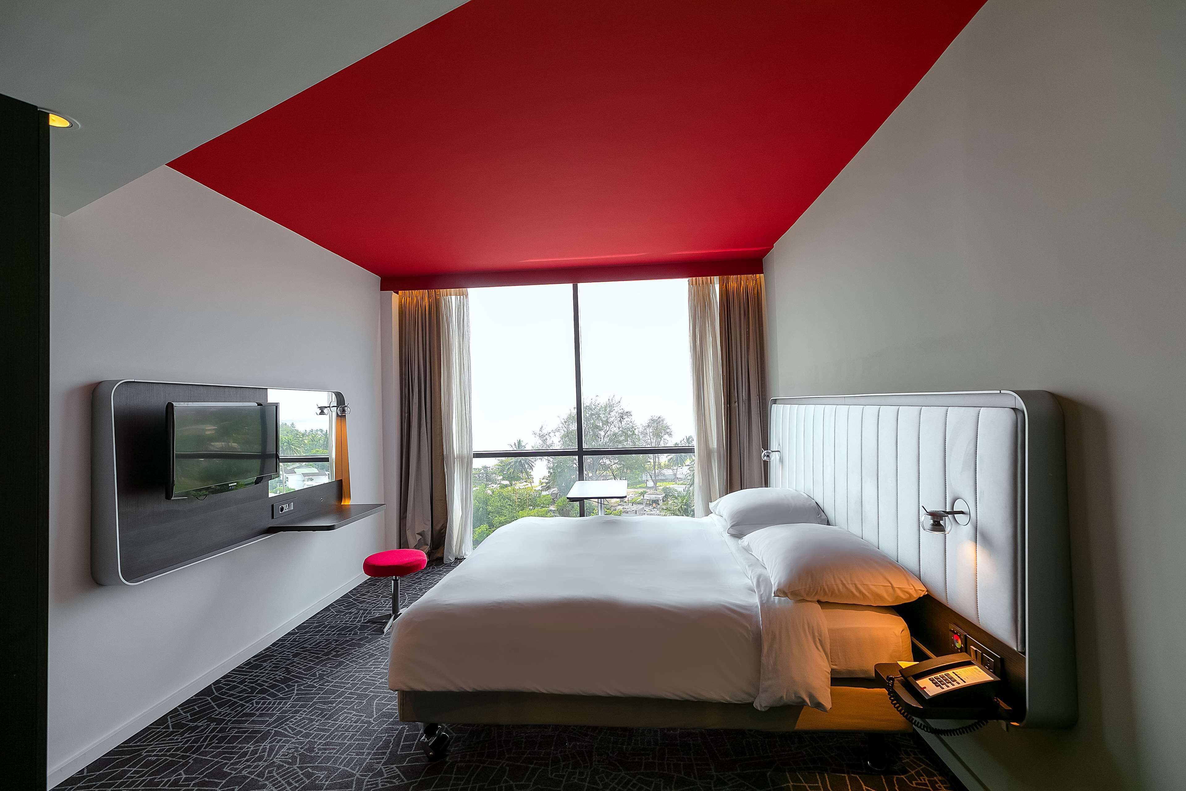 A modern hotel room with a large bed, a mounted TV, and a telephone.