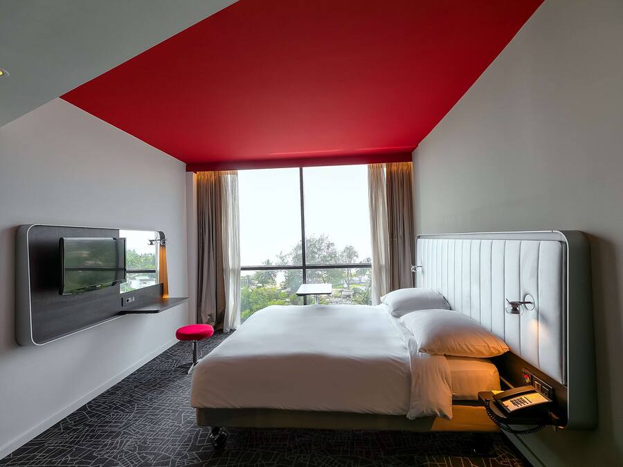 A modern hotel room with a large bed, a mounted TV, and a telephone.