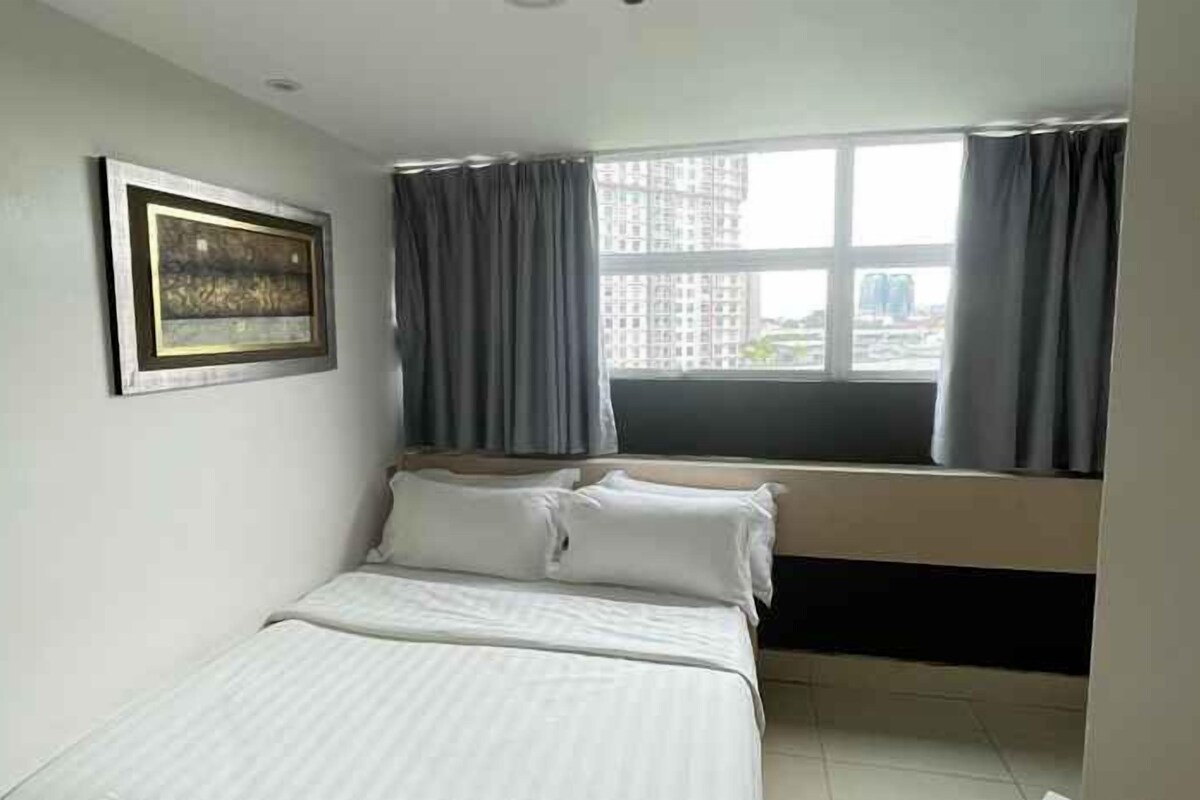 A bedroom with a bed, a window with curtains, and a framed picture on the wall.
