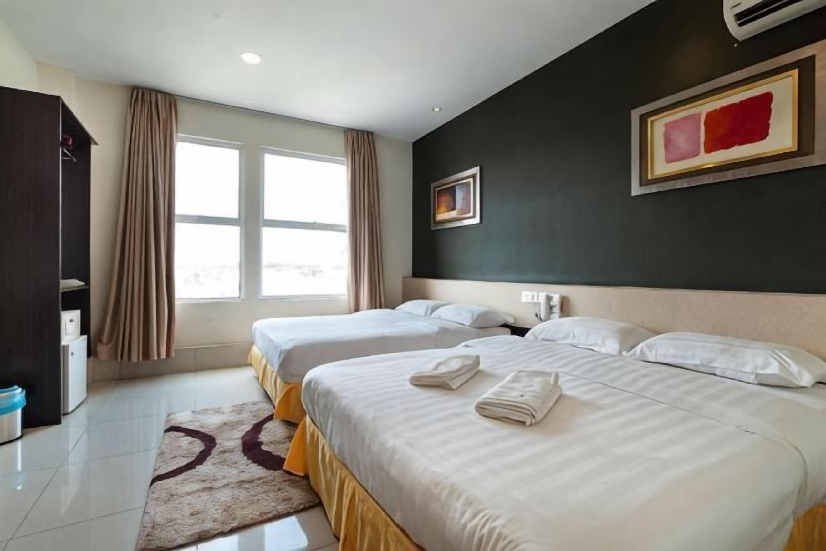 A hotel room with two beds, a large window, a dark wall with a painting, and a white ceiling.