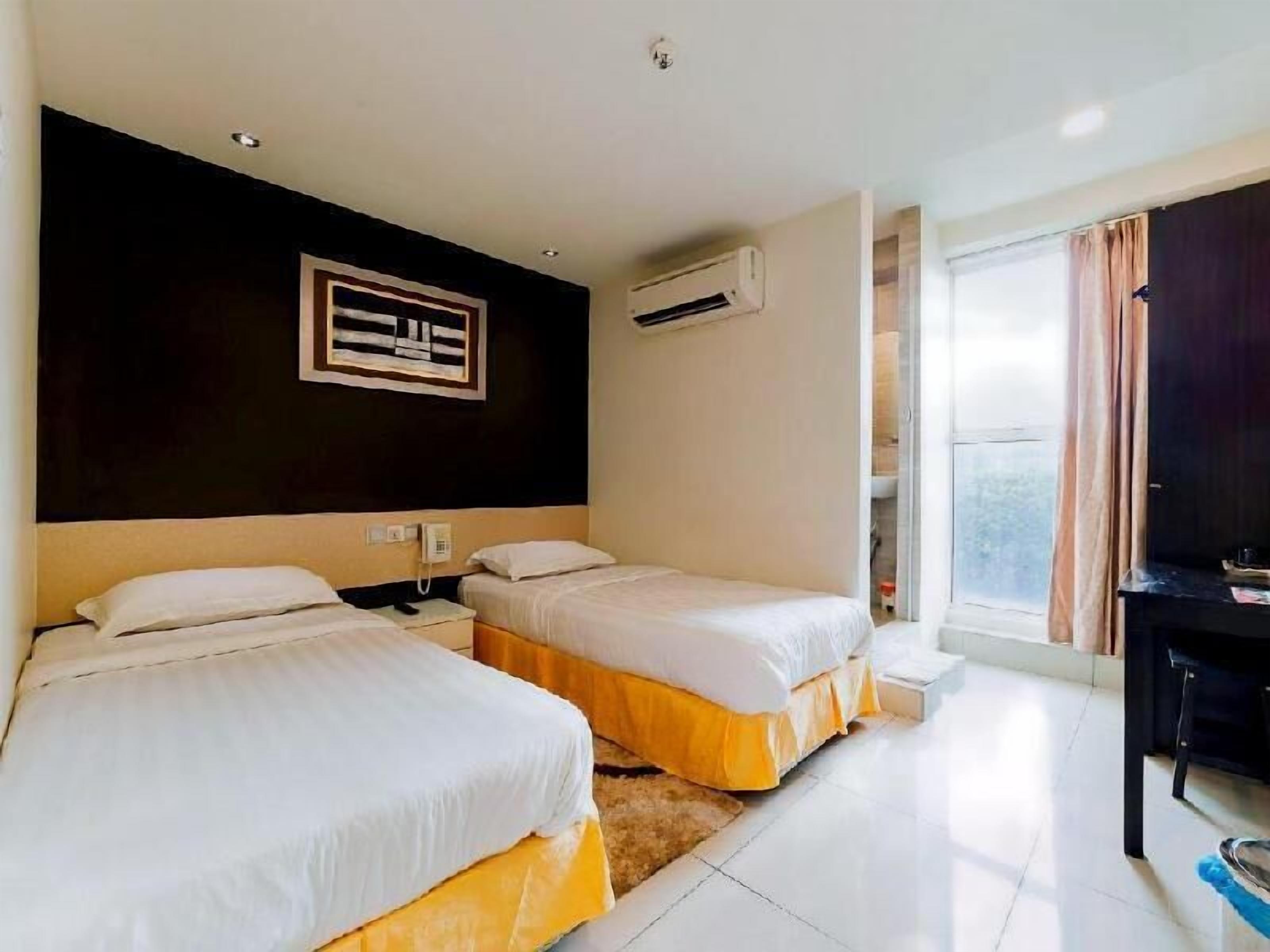 Habitación de hotel con dos camas, un escritorio, una silla, un ventanal con cortinas y un equipo de aire acondicionado.