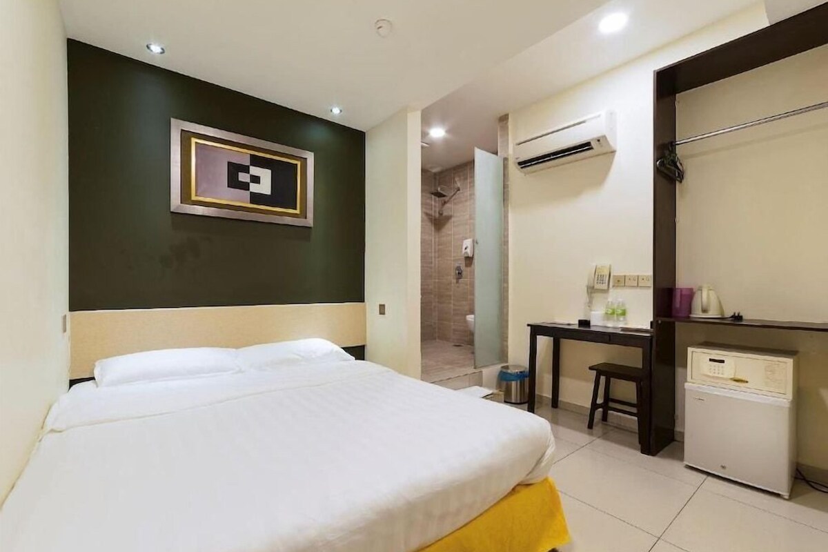 A hotel room with a bed, a desk, a mini-fridge, and an air conditioning unit.