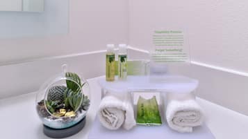 A bathroom with a white sink, a glass dome containing a cactus and succulents, a bottle of shampoo, a bottle of conditioner, and a sign with hotel promises.