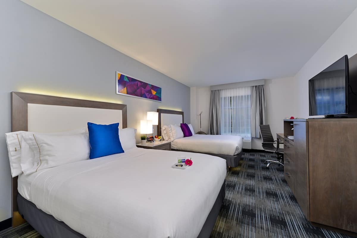 A hotel room with two beds, a desk, a television, and a painting on the wall.
