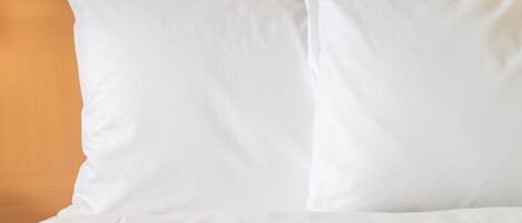 A bed with white bedding and pillows against a wooden headboard.