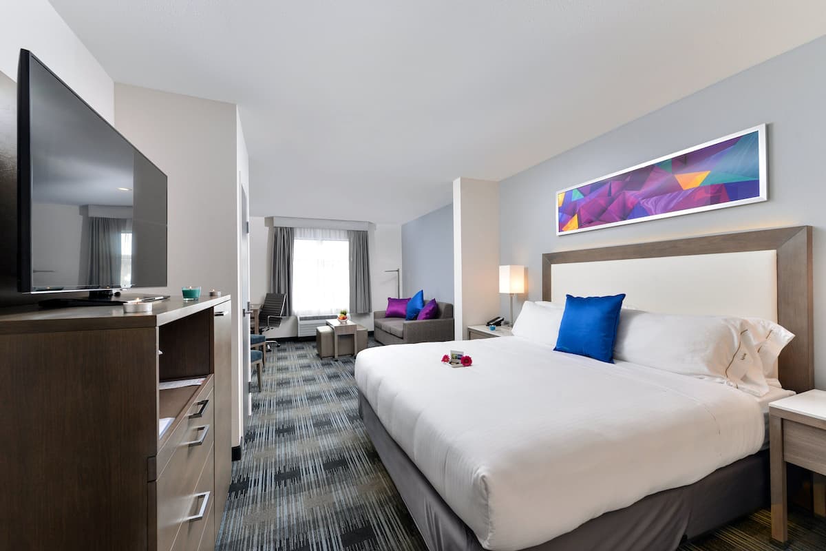 A hotel room with a large bed, a TV, a desk, and a modern art piece on the wall.