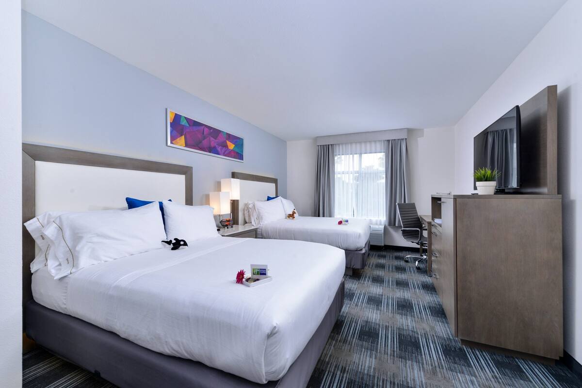 A hotel room with two beds, a desk, a TV, and a painting on the wall.