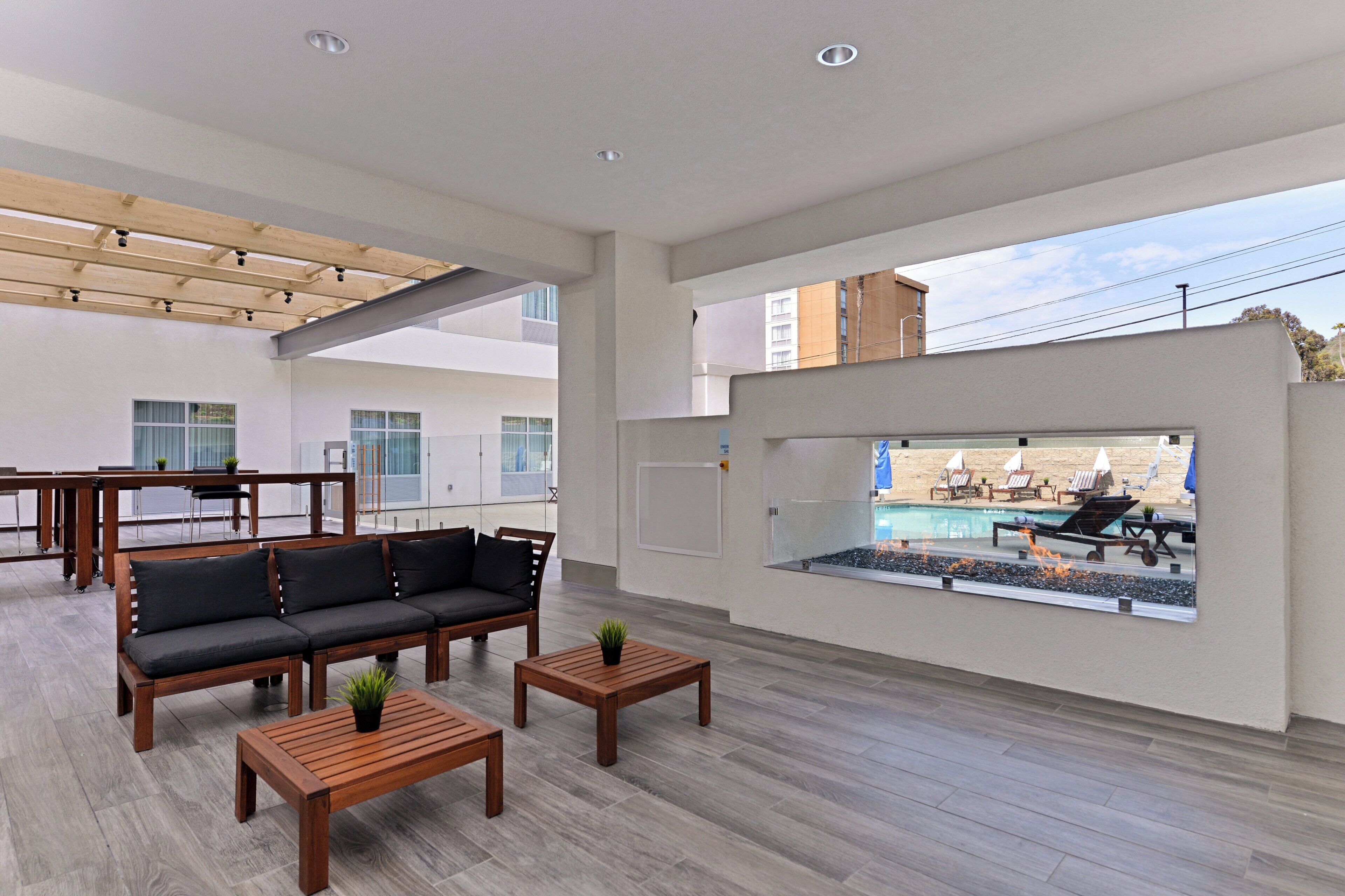 A spacious outdoor area with a pool, wooden furniture, and a view of the city.