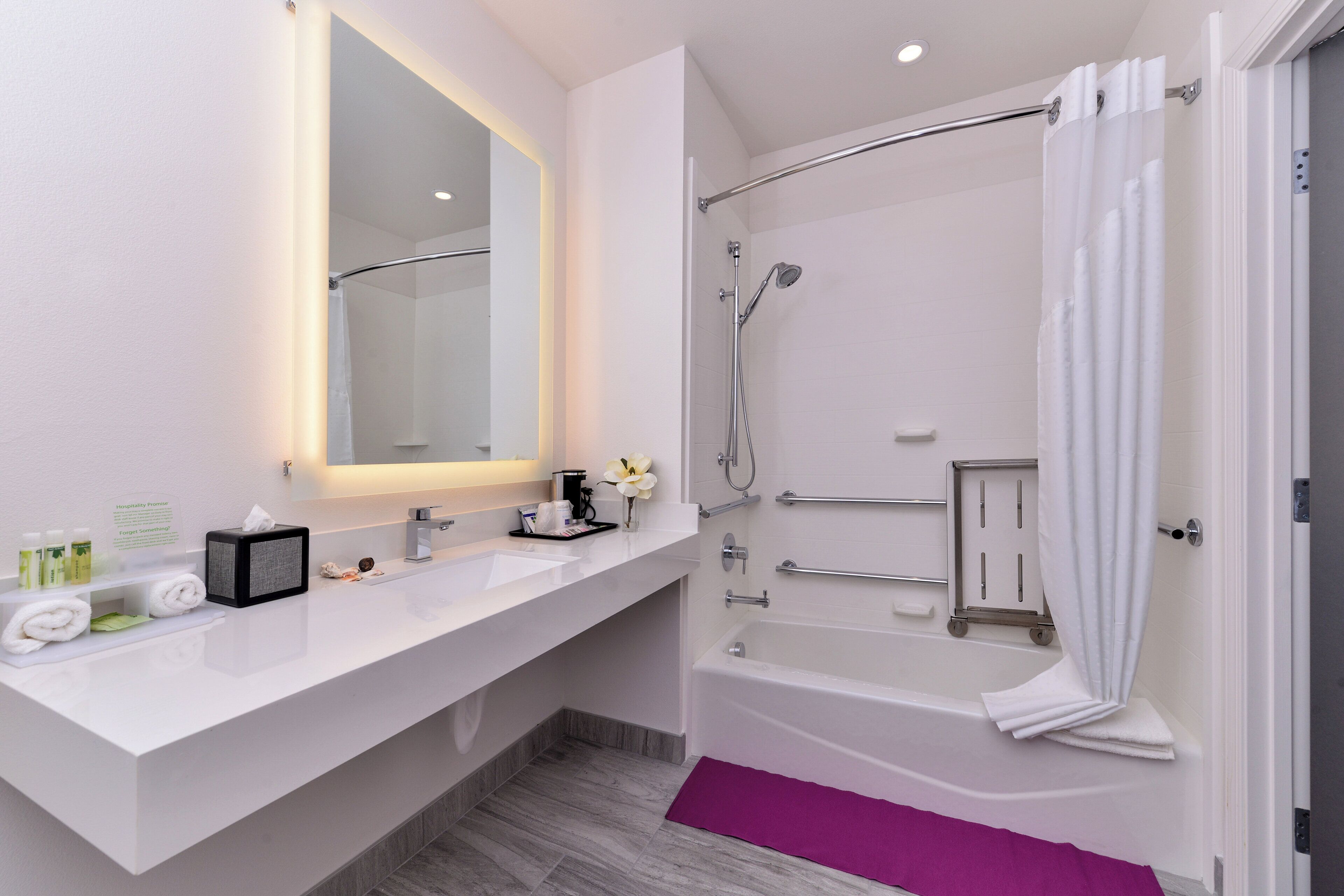 Un baño moderno con tocador blanco, un espejo grande, ducha con cabezal de ducha manual y una bañera.