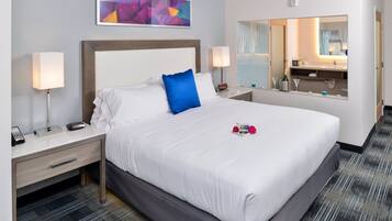 A hotel room with a large bed, two bedside tables, a nightstand, a mirror, and a window.