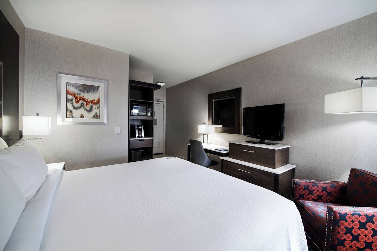 Ein Hotelzimmer mit einem großen Bett, einem Schreibtisch mit Stuhl, einem Fernseher und einer Mikrowelle.
