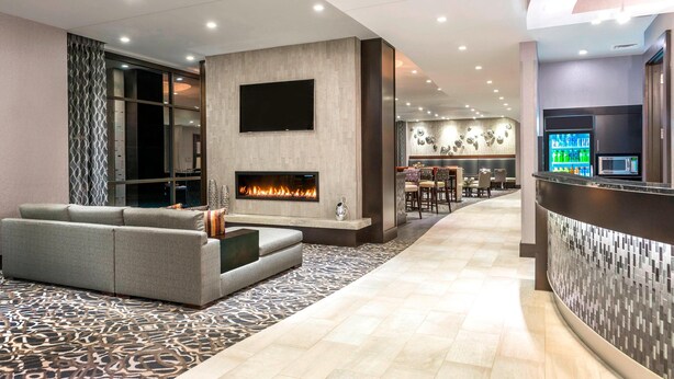 A modern lobby with a fireplace, seating area, and a bar. - Fairfield Inn & Suites Boston Cambridge (Cambridge)