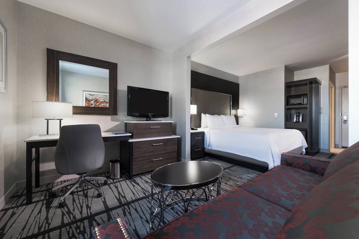 Ein Hotelzimmer mit Bett, Schreibtisch mit Stuhl, Fernseher, Sofa und einem kleinen Tisch.