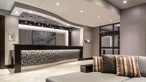A modern reception area with a curved reception desk, a large abstract painting, and a seating area with a sofa and cushions. - Fairfield Inn & Suites Boston Cambridge (Cambridge)