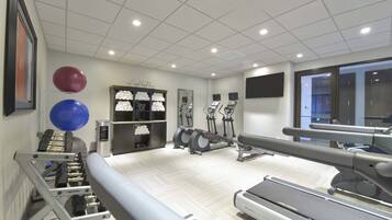 A gym with exercise equipment, including treadmills and ellipticals, and a wall-mounted TV.