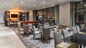 A modern hotel lobby with a bar area, seating arrangements, and large windows. - Fairfield Inn & Suites Boston Cambridge (Cambridge)