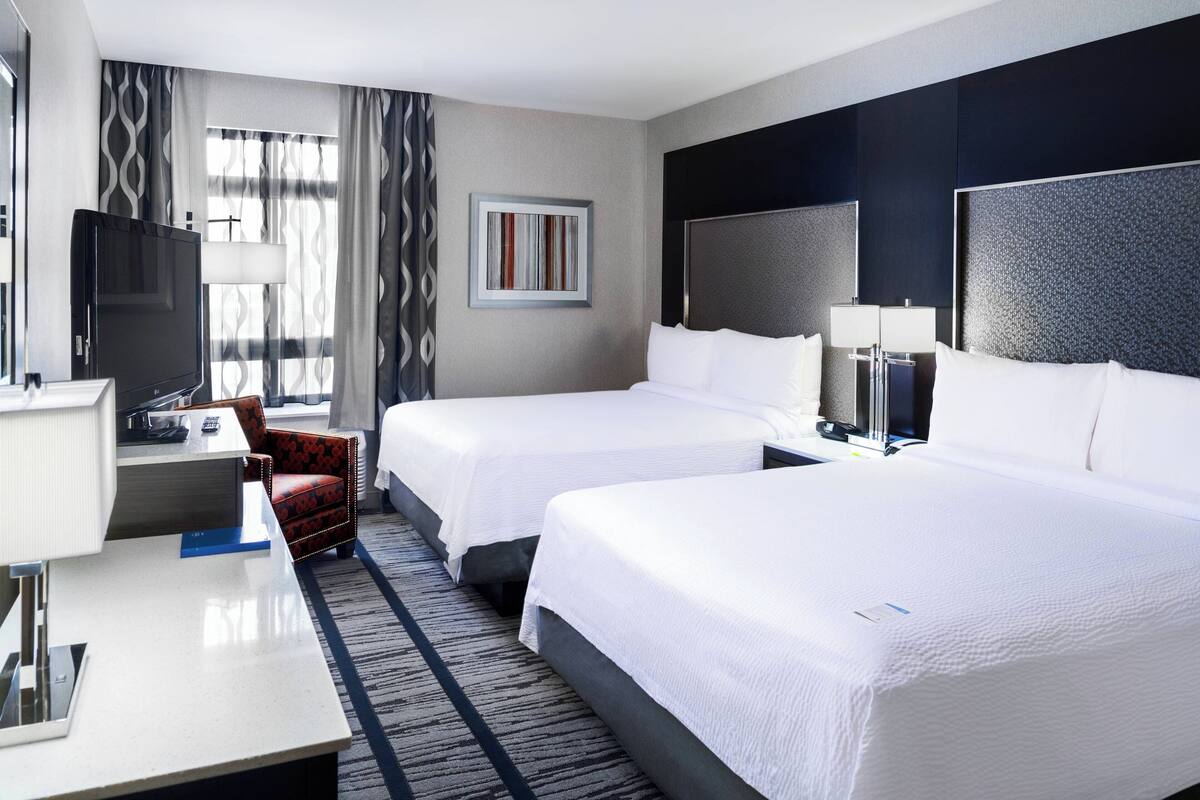 Ein Hotelzimmer mit zwei Betten, einem Schreibtisch, einem Computer, einem Fernseher und einem Sessel.
